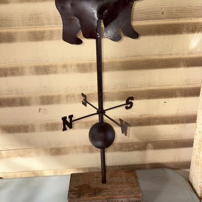 Sale Photo Thumbnail #68: 24in long.
A decorative metal weather vane featuring a silhouette of a bear topper with directional markers (N, S, E, W) and a central globe. Mounted on a rectangular wooden block base. Shows light wear and patina consistent with age and use.