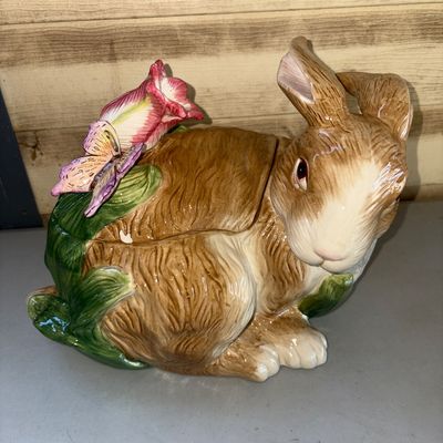 Sale Photo Thumbnail #234: Decorative hand-painted glazed ceramic rabbit cookie jar or covered dish featuring a butterfly and pink flower on the removable lid. Shows a small paint chip/flake on the rim under the lid area as visible in close-up photos. Otherwise in good overall cond