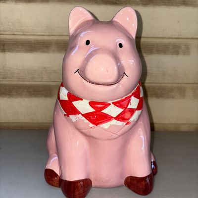 Sale Photo Thumbnail #193: Pink glazed ceramic pig cookie jar featuring a smiling face, red and white checkered neck scarf/bandana, and brown hooves. Removable head lid. Shows light wear to the paint around the neck area, otherwise appears in good condition with no visible cracks o