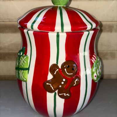 Sale Photo Thumbnail #197: Festive ceramic Christmas cookie jar with lid, featuring red, green, and white stripes, relief gingerbread man, and present accents. Clean interior with no visible cracks or major chips. Great holiday kitchen decor item.
13in tall