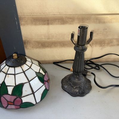 Sale Photo Thumbnail #352: Small table lamp featuring a leaded/stained glass style shade with pink floral motifs and green leaves against white panels. Includes a dark cast metal base with decorative floral patterns and an inline power switch. The shade is detached from the base as