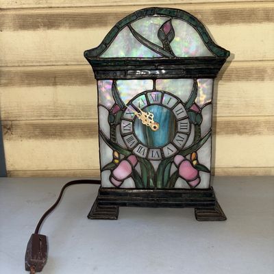 Sale Photo Thumbnail #228: Vintage stained glass clock in a Tiffany-style arched mantle casing featuring opalescent and floral glass panels with Roman numerals on the clock face. Features a rear access door. Please note condition: power cord end is damaged/cut and requires repair/r