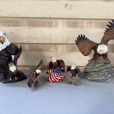 Sale Photo Thumbnail #57: A collection of 6 resin bald eagle decorative figurines in various poses, including an eagle perching on an American flag, eagles in flight, and perched eagles. Overall good condition with detailed painting. Material appears to be molded resin or composit