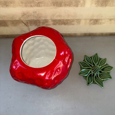 Sale Photo Thumbnail #173: Ceramic strawberry-shaped cookie jar featuring a bright red glazed body with textured seed dimples and a green leaf-and-stem lid. Features a glossy glazed interior. Good pre-owned condition with no visible cracks or large chips.
11in tall