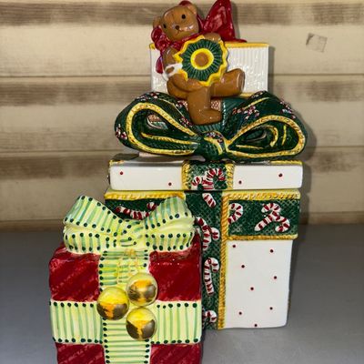 Sale Photo Thumbnail #187: Hand-painted ceramic festive table decor set featuring a stacked gift box cookie jar/container adorned with a teddy bear, a girl holding a 'Happy Holidays' sign, candy canes, and festive bows, accompanied by a smaller matching gift box ceramic piece. Appe