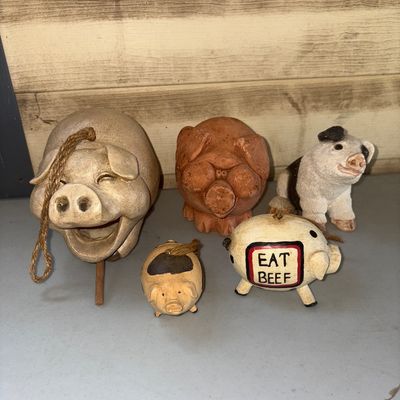 Sale Photo Thumbnail #295: A collection of five whimsical pig-themed decorative items. Includes a large ceramic or clay hanging pig bell with wooden clapper and rope hanger, a terracotta-style stylized pig figurine, a painted pig featuring an "EAT BEEF" sign on its side, and two sm