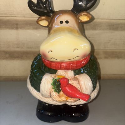 Sale Photo Thumbnail #252: Charming ceramic holiday cookie jar featuring a smiling moose wearing a green winter coat and red scarf, holding a red cardinal. Features a removable lid. High-gloss finish. Good overall condition with no visible cracks or major chips.
12in tall