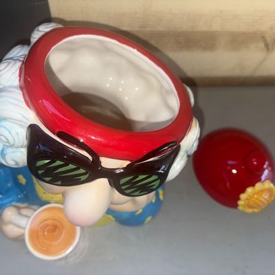 Sale Photo Thumbnail #242: Ceramic novelty cookie jar depicting an elderly character wearing sunglasses and a red beanie with a flower, holding a coffee mug that reads "YOU AGAIN?". Brightly painted glazed ceramic finish. Appears in good overall condition with no visible chips or c