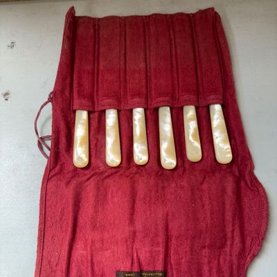 Sale Photo Thumbnail #334: Set of six antique flatware spreaders featuring mother of pearl handles and sterling silver ferrule details, housed in their original red cloth storage roll pouch labeled 'R. Wallace & Sons Mfg. Co., Wallingford, Conn.'. Light surface patina consistent wi