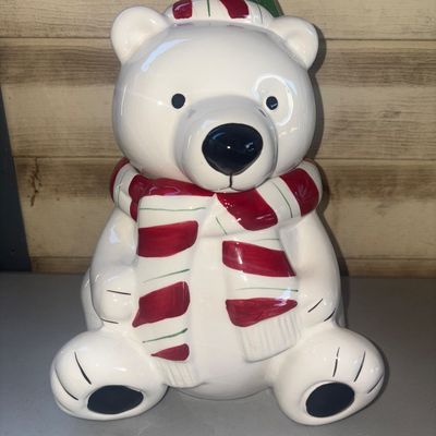 Sale Photo Thumbnail #250: Ceramic holiday cookie jar shaped like a seated polar bear wearing a red and white striped scarf and a green hat. Features a removable head lid with a painted finish. Clean interior, gently used with no visible cracks or chips.
11in tall