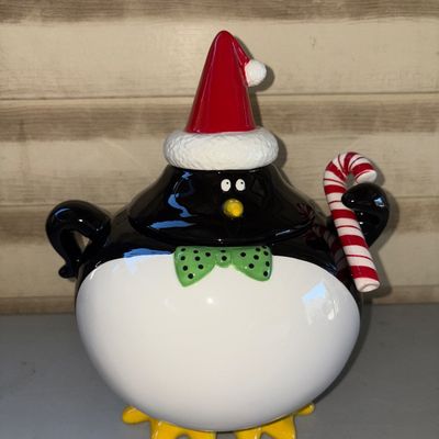 Sale Photo Thumbnail #199: Ceramic festive penguin-shaped cookie jar featuring a Santa hat lid, green polka dot bow tie, and holding a candy cane. The piece has a glossy painted finish. In good pre-owned condition with no visible chips or cracks.
11in tall