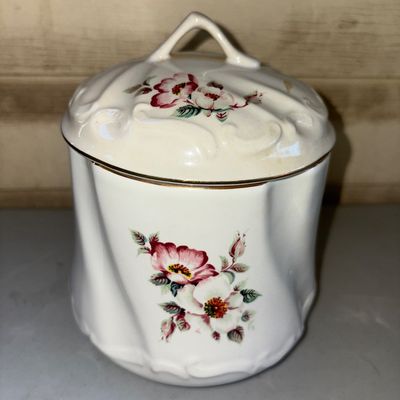 Sale Photo Thumbnail #184: Lidded ceramic or porcelain container featuring a molded swirl pattern, gilded trim, and pink floral rose motifs. Appears in good overall condition with minor wear to the gilt accent trim.
7in tall