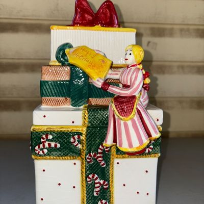Sale Photo Thumbnail #188: Hand-painted ceramic festive table decor set featuring a stacked gift box cookie jar/container adorned with a teddy bear, a girl holding a 'Happy Holidays' sign, candy canes, and festive bows, accompanied by a smaller matching gift box ceramic piece. Appe