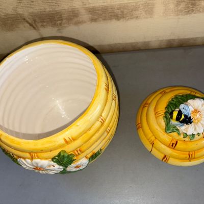 Sale Photo Thumbnail #175: Ceramic beehive-shaped cookie jar or canister featuring relief daisy flowers and a bumblebee finial on the lid. Bright yellow glazed finish with hand-painted details. Good condition with minor surface wear consistent with age and use.
10in tall