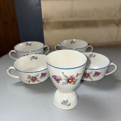 Sale Photo Thumbnail #317: A 5-piece vintage porcelain tableware set decorated with colorful floral motifs and blue trim. Includes one pedestal egg cup and four double-handled bouillon or soup cups. Overall good vintage condition with no visible chips or cracks. Light discoloration
