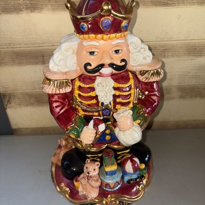 Sale Photo Thumbnail #269: Hand-painted ceramic Christmas nutcracker king cookie jar featuring a removable lid, gold gilt trim details, and toy motifs at the base. Good condition with glossy finish and no visible major chips or cracks.
13in tall