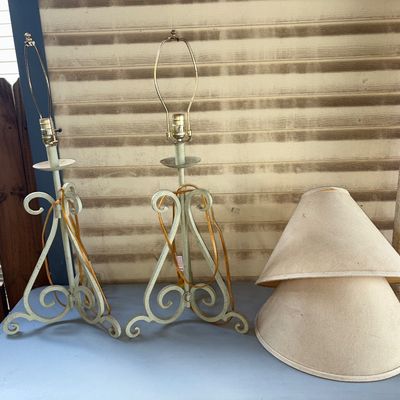 Sale Photo Thumbnail #393: Pair of metal table lamps featuring scrollwork bases with a cream/light green painted finish. Includes two conical fabric lampshades with finial harps. Condition: Lamps show light surface wear; one lampshade has a split/separation along the top rim edge a