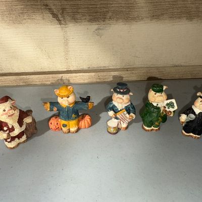Sale Photo Thumbnail #61: A collection of five resin or cold-cast ceramic pig figurines depicting various holidays and themes: Santa Claus (Christmas), scarecrow with pumpkins (Halloween/Autumn), Uncle Sam with drum (4th of July), leprechaun with shamrock (St. Patrick's Day), and 