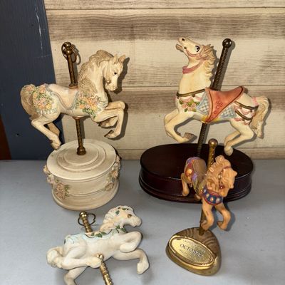 Sale Photo Thumbnail #312: Collection of four carousel horse themed decorative items, including a musical carousel horse on a round base decorated with floral details, a carousel horse mounted on a dark wooden base, a smaller Willitts Designs 'October' carousel horse figurine, and 