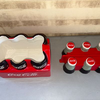 Sale Photo Thumbnail #190: Ceramic Coca-Cola cookie jar designed as a classic red 6-pack bottle carrier with removable bottle top lid. Features bright glazed finish and Coca-Cola branding. Shows minor signs of handling but overall good condition with no major chips or cracks visibl