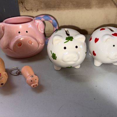 Sale Photo Thumbnail #27: Collection of pig-themed items including a ceramic pig mug with blue patterned handle, two small ceramic piggy banks (one with red hearts, one with green shamrocks), a small pig keychain, and a small pig figure. Note: The shamrock piggy bank has a visible