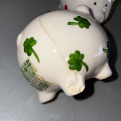 Sale Photo Thumbnail #28: Collection of pig-themed items including a ceramic pig mug with blue patterned handle, two small ceramic piggy banks (one with red hearts, one with green shamrocks), a small pig keychain, and a small pig figure. Note: The shamrock piggy bank has a visible