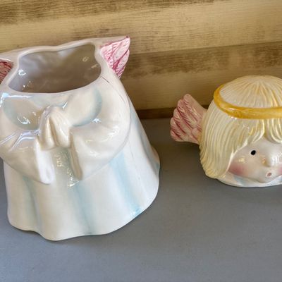 Sale Photo Thumbnail #166: Charming ceramic praying angel cookie jar with lid. Features pastel blue and white robes, blonde hair with a yellow halo, and pink feathered wings. Glazed finish. Shows light wear consistent with age, including subtle hairline cracking near the top rim of