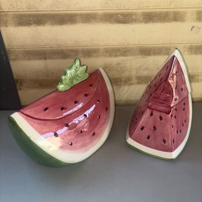 Sale Photo Thumbnail #245: Set of two glazed ceramic decorative containers shaped like watermelon slices, complete with removable lids. One features a green leaf handle on top, and the other is styled as an upright slice. Shiny glazed finish in pink, green, and white with painted s