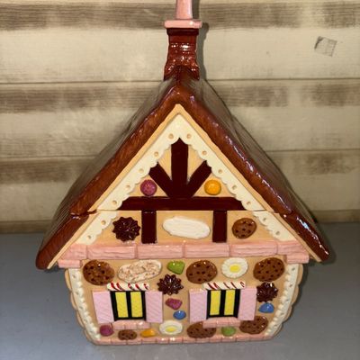 Sale Photo Thumbnail #170: Ceramic or painted earthenware cookie jar shaped like a gingerbread house with candy and cookie details. Features a removable roof lid with chimney handle. Glossy glazed finish. Appears to be in good condition with no visible cracks or chips.
14in tall