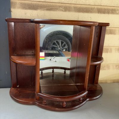 Sale Photo Thumbnail #313: A dark wood wall-hanging display shelf featuring a central mirror back, spindle rail accents on the lower shelf, and two curved side tiers. Shows light surface wear and minor dust consistent with age and use.
13X20in