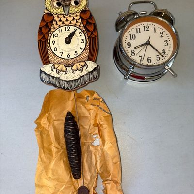 Sale Photo Thumbnail #13: Pair of vintage timepieces featuring a wood-look novelty owl-shaped wall clock with a pinecone weight pendulum and a classic chrome-finished twin bell alarm clock. Items show light wear consistent with age. Functionality has not been tested.
Owl is 8X4in
