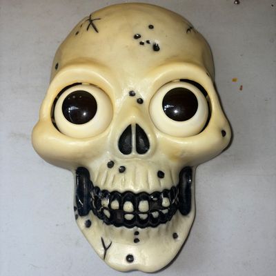 Sale Photo Thumbnail #373: Molded plastic skull Halloween wall decoration featuring googly/moving eyes and internal speaker. Back marked Playhut and Made in China. Requires 4 AA batteries (not included). Shows minor surface wear, scuffs, and residue on the back panel.
10X7in