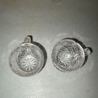 Sale Photo Thumbnail #210: Pair of clear pressed or cut glass cups featuring intricate diamond geometric patterns, textured handles, and starburst bases. Ideal for punch, tea, or decorative use. Both pieces appear to be in good condition with minor surface wear consistent with age 
