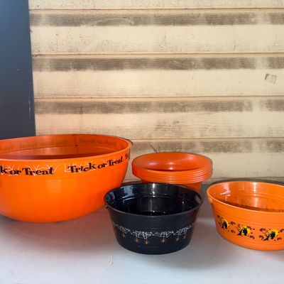Sale Photo Thumbnail #365: Collection of plastic Halloween candy bowls and bucket containers, including a large orange 'Trick or Treat' serving bowl, a black spiderweb design bowl, a small orange Halloween motif oval bucket with handles, and stacked orange small bowls. Items appear