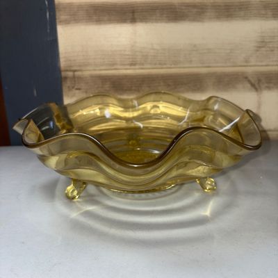 Sale Photo Thumbnail #310: Vintage yellow amber glass bowl featuring a crimped/ruffled edge and three small feet. The center base exhibits a molded starburst/sunburst pattern. Appears to be in good condition with no visible chips or cracks.
10in