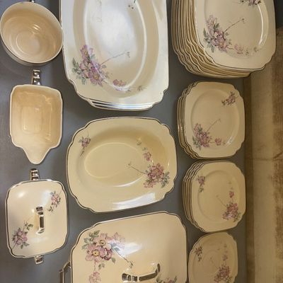 Sale Photo Thumbnail #281: Comprehensive vintage ceramic/china dinnerware service featuring a cream-colored base with delicate pink floral motifs and metallic trim accenting the scalloped edges. Includes a large covered casserole/tureen, covered sugar bowl, creamer, open vegetable 