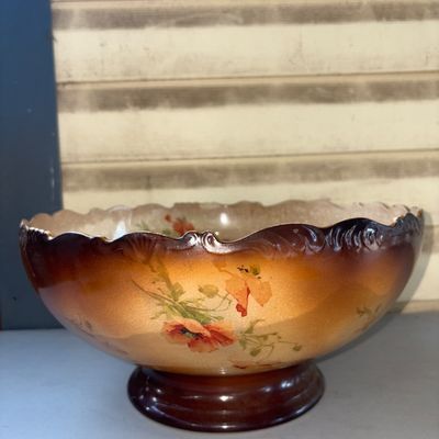 Sale Photo Thumbnail #382: Large antique ceramic or earthenware footed bowl featuring a scalloped rim and a shaded brown-to-tan glaze. Decorated with hand-painted or transfer floral poppy designs on one side and an interior, and a portrait of a monk drinking beer/ale on the opposit