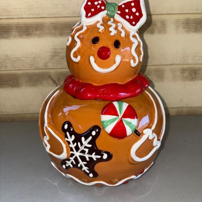 Sale Photo Thumbnail #182: Glazed ceramic gingerbread girl cookie jar featuring festive holiday details including a red polka dot bow, peppermint swirl, and snowflake icing accents. Consists of a base container and removable head lid. In good pre-owned condition with shiny glaze fi