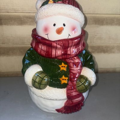 Sale Photo Thumbnail #254: A festive ceramic snowman cookie jar featuring a green jacket, red scarf, winter hat, and star buttons. Clean interior, overall good condition with no visible cracks or chips.
11in tall