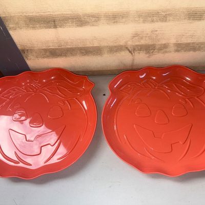 Sale Photo Thumbnail #371: A pair of matching bright orange molded plastic Halloween serving platters or trays featuring raised jack-o'-lantern face designs with leaf and stem accents at the top. Ideal for serving snacks or candy during Halloween festivities. Appears to be in good 