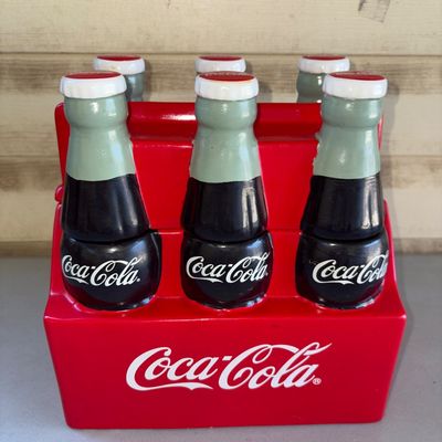 Sale Photo Thumbnail #189: Ceramic Coca-Cola cookie jar designed as a classic red 6-pack bottle carrier with removable bottle top lid. Features bright glazed finish and Coca-Cola branding. Shows minor signs of handling but overall good condition with no major chips or cracks visibl