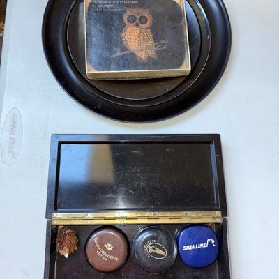 Sale Photo Thumbnail #35: Vintage Mid-Century Couroc of Monterey resin table accessory set featuring an owl design with inlaid brass/gold-tone stars and branch details. Includes a hinged rectangular box, a boxed set of six 'Conversation Coasters', and a round black serving tray. I