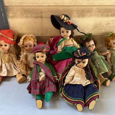 Sale Photo Thumbnail #46: A collection of 7 vintage small sleep-eye dolls dressed in various traditional, regional, and international costumes, including Scottish tartan attire and wide-brimmed hats. Plastic and fabric construction. Minor wear consistent with age, including stray 
