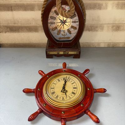 Sale Photo Thumbnail #33: Set of two maritime-themed decorative clocks including a ship's wheel shaped clock with Roman numerals and a table clock featuring a rope border, map face design, knot accents, and brass trim. Made of wood, brass tone metal, and rope elements. Both show l