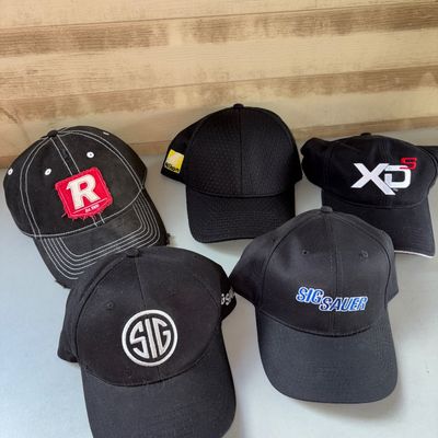 Sale Photo Thumbnail #101: A group of 5 black baseball caps featuring various logos and promotional embroidery, including Sig Sauer, Sig, Springfield XDs, and Nikon. Caps appear gently pre-owned with light signs of wear. Adjustable sizing.