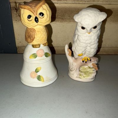 Sale Photo Thumbnail #15: A pair of decorative ceramic owl figurines, including one owl perched on a floral painted bell and one white snowy owl perched on a branch. Both pieces feature hand-painted details and textured ceramic finishes. Appears to be in good vintage condition wit