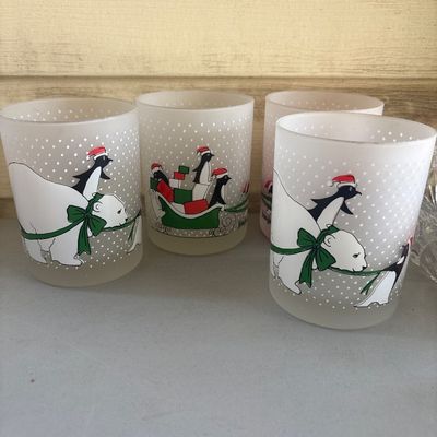 Sale Photo Thumbnail #282: Set of 4 festive frosted glass tumblers or votive holders featuring a holiday scene of penguins riding in a sleigh pulled by a polar bear with a polka dot snow background. Appears to be in good pre-owned condition with no visible chips or cracks. Each gla