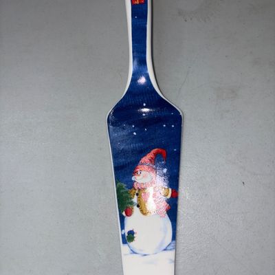 Sale Photo Thumbnail #315: Ceramic pie or cake server featuring a festive winter snowman scene on a dark blue background with gift motif on the handle. Excellent condition with glossy finish and no visible chips or cracks.