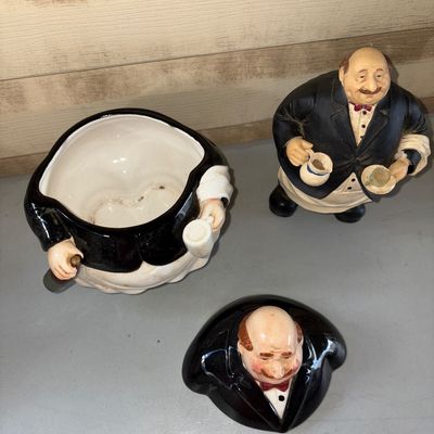 Sale Photo Thumbnail #53: 8.5X5.5in on cookie jar
8in tall on figure 
Pair of whimsical kitchen/bistro decor items featuring a ceramic waiter/chef cookie jar with removable lid and a matching resin waiter figurine. Items show light surface wear and minor discoloration on the apron