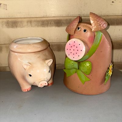 Sale Photo Thumbnail #23: Pair of novelty pig-themed decorative items. Includes one ceramic pig-shaped planter or holder with an open top and one painted metal pig watering can featuring a green bow and flower accent. Both items show mild surface wear consistent with light use.
6X